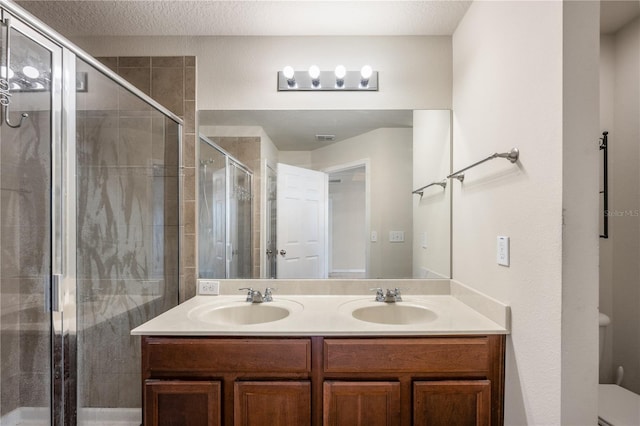 full bathroom featuring a sink, a textured ceiling, a stall shower, and double vanity