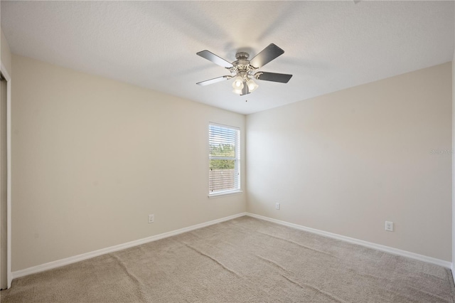 empty room featuring light colored carpet, a ceiling fan, and baseboards