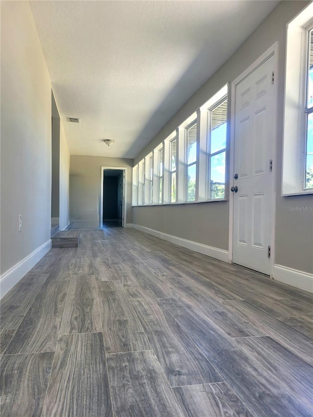 unfurnished living room with a textured ceiling, a healthy amount of sunlight, and dark wood-type flooring