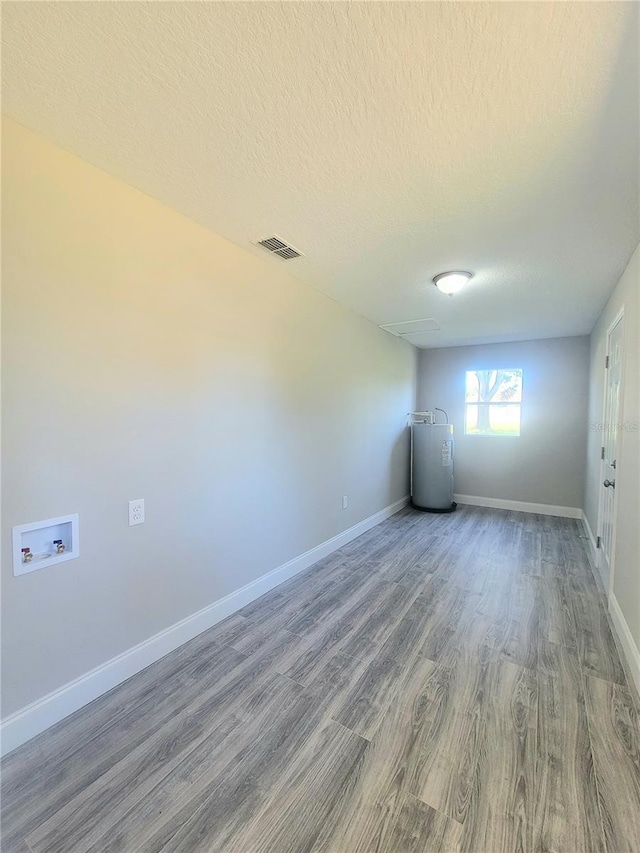 unfurnished room with wood-type flooring, a textured ceiling, and water heater