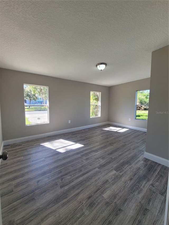 empty room featuring dark wood-type flooring, a healthy amount of sunlight, and a textured ceiling