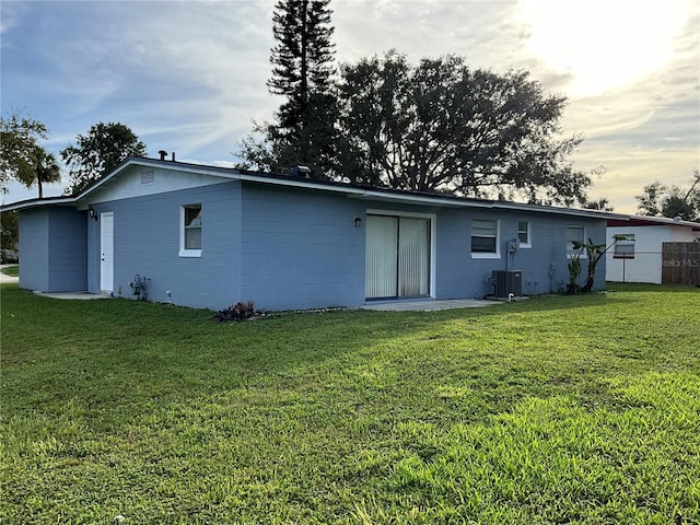 back house at dusk with central air condition unit and a lawn