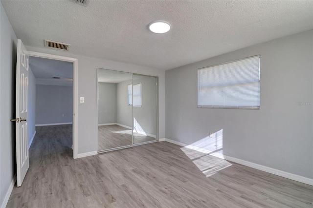 unfurnished bedroom featuring a closet, a textured ceiling, and light hardwood / wood-style flooring