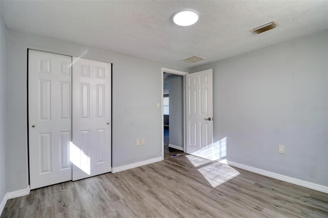 unfurnished bedroom with light wood-type flooring, a textured ceiling, and a closet