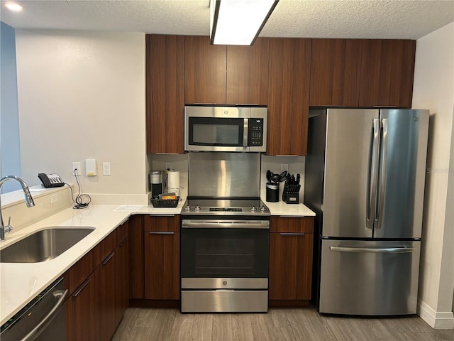 kitchen featuring sink, appliances with stainless steel finishes, light hardwood / wood-style flooring, and a textured ceiling