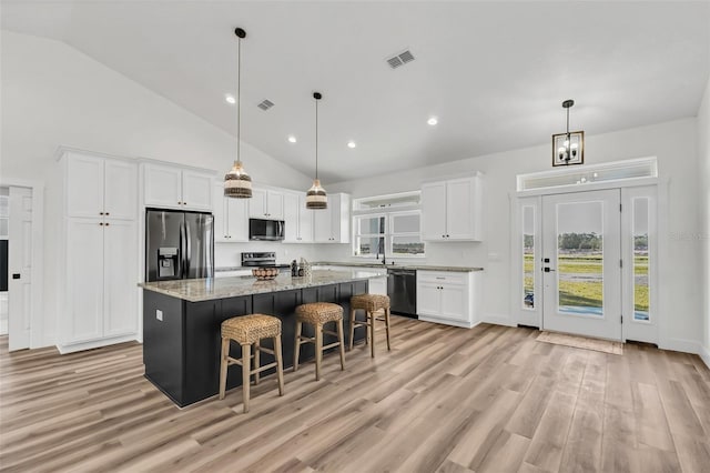 kitchen with white cabinets, light stone counters, light hardwood / wood-style flooring, stainless steel appliances, and a center island