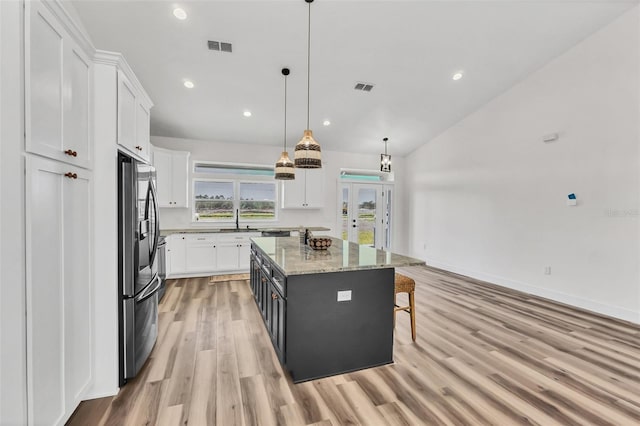 kitchen featuring white cabinets, stainless steel fridge with ice dispenser, a kitchen island, pendant lighting, and light hardwood / wood-style floors