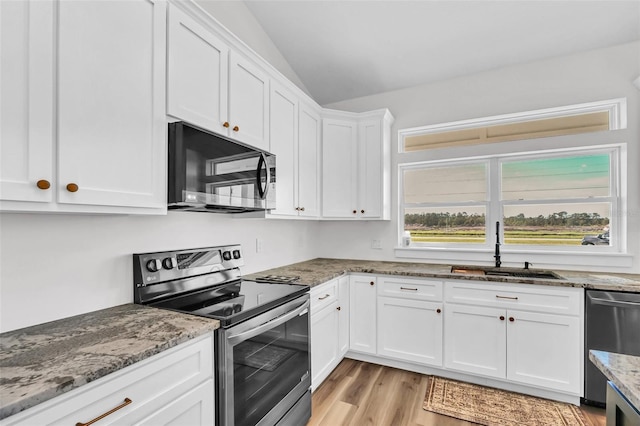 kitchen featuring stone counters, appliances with stainless steel finishes, vaulted ceiling, white cabinets, and light hardwood / wood-style flooring