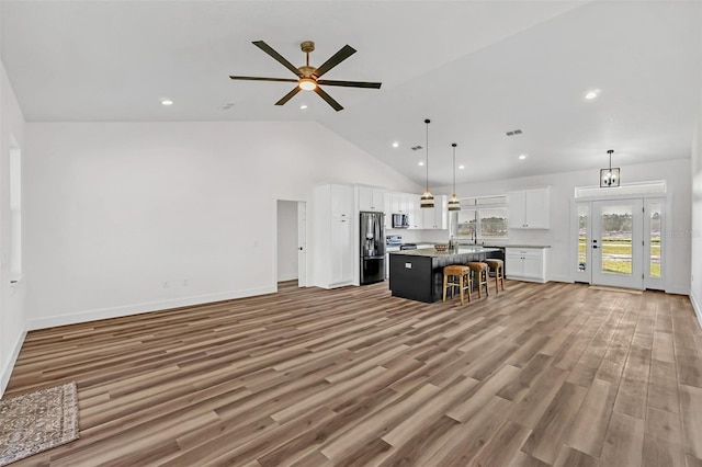 kitchen with appliances with stainless steel finishes, light hardwood / wood-style floors, decorative light fixtures, white cabinets, and a kitchen island with sink