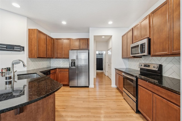 kitchen featuring appliances with stainless steel finishes, light wood-type flooring, dark stone countertops, and sink