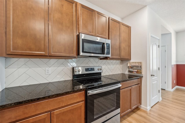 kitchen featuring backsplash, dark stone countertops, a textured ceiling, appliances with stainless steel finishes, and light wood-type flooring