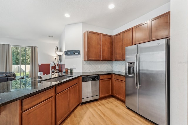 kitchen featuring sink, kitchen peninsula, light hardwood / wood-style floors, dark stone counters, and appliances with stainless steel finishes