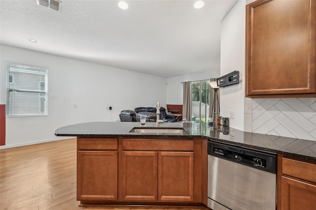 kitchen with light hardwood / wood-style floors, stainless steel dishwasher, dark stone countertops, and sink