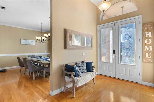 entrance foyer with hardwood / wood-style floors, ornamental molding, a chandelier, and french doors