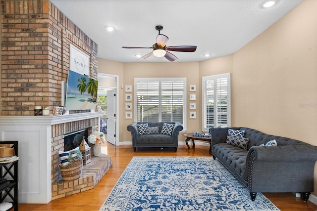 living room featuring a brick fireplace, light wood-type flooring, and ceiling fan