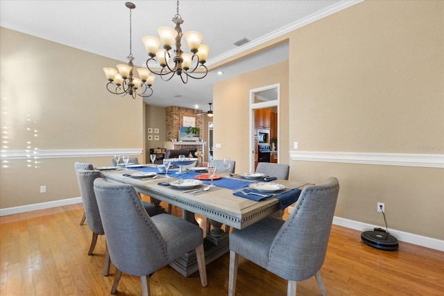 dining space featuring crown molding, light hardwood / wood-style flooring, a fireplace, and ceiling fan with notable chandelier