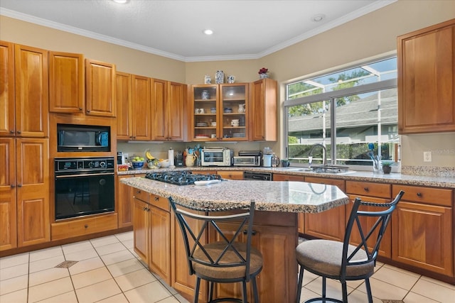 kitchen featuring black appliances, a kitchen island, light stone counters, ornamental molding, and a breakfast bar