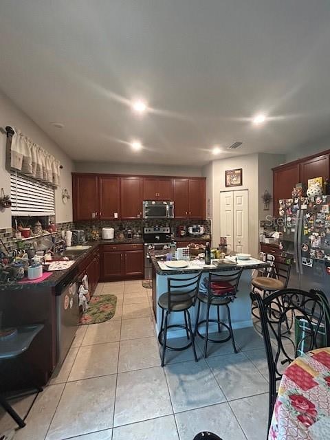 kitchen featuring a kitchen bar, decorative backsplash, light tile patterned floors, and stainless steel appliances