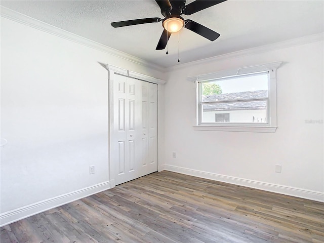 unfurnished bedroom with dark wood-type flooring, crown molding, a closet, and ceiling fan