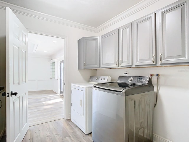 washroom featuring ornamental molding, separate washer and dryer, light hardwood / wood-style floors, and cabinets