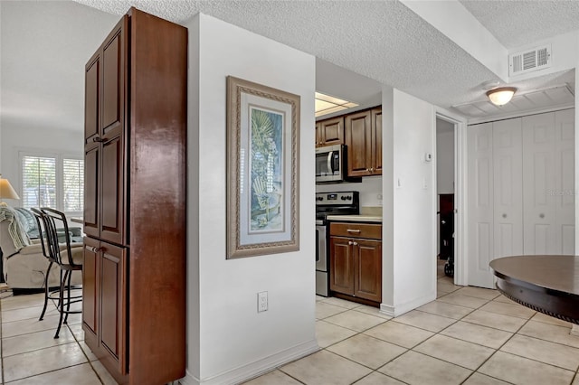 kitchen with appliances with stainless steel finishes, a textured ceiling, and light tile patterned floors