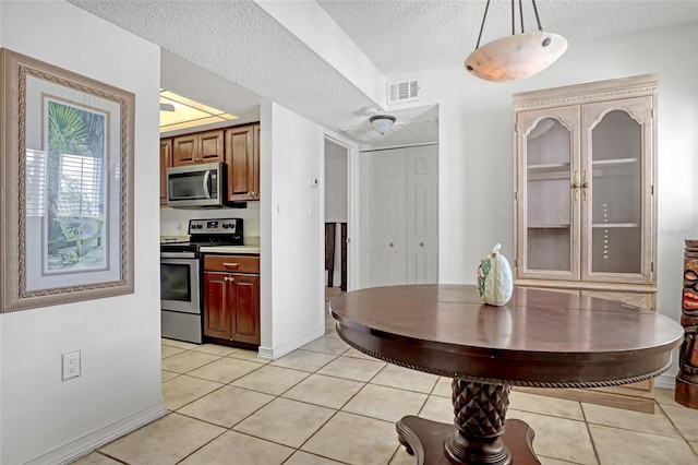 kitchen with a textured ceiling, hanging light fixtures, stainless steel appliances, and light tile patterned floors