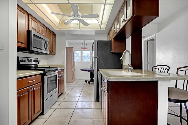 kitchen with ceiling fan, appliances with stainless steel finishes, a kitchen breakfast bar, light tile patterned flooring, and sink