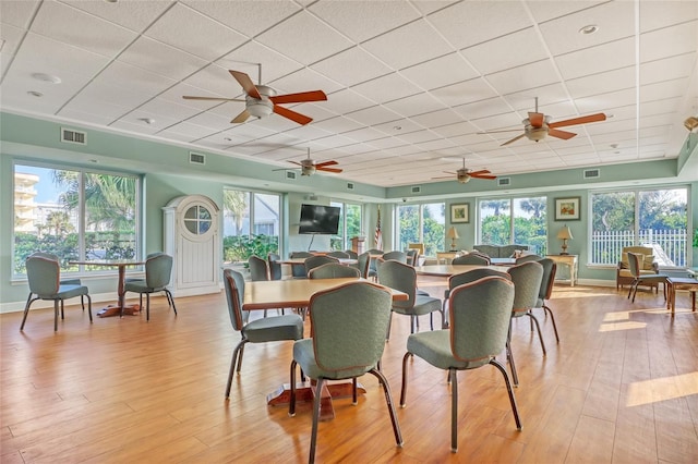 dining area featuring light wood-type flooring, a drop ceiling, and plenty of natural light