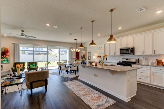 kitchen with gas stove, white cabinets, a center island with sink, dark hardwood / wood-style flooring, and a kitchen bar