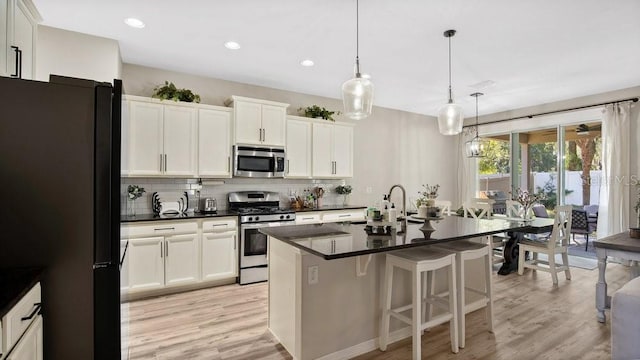 kitchen with white cabinets, hanging light fixtures, backsplash, an island with sink, and stainless steel appliances