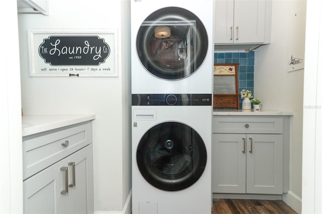 clothes washing area featuring stacked washer / drying machine, dark wood-type flooring, and cabinets