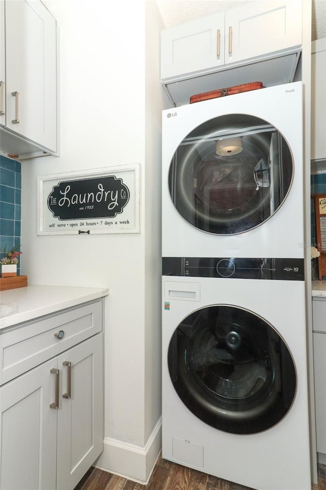 laundry room with cabinets, stacked washer / drying machine, and dark hardwood / wood-style flooring