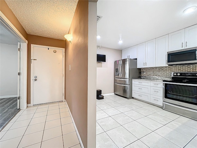 kitchen with backsplash, a textured ceiling, stainless steel appliances, white cabinets, and light tile patterned floors