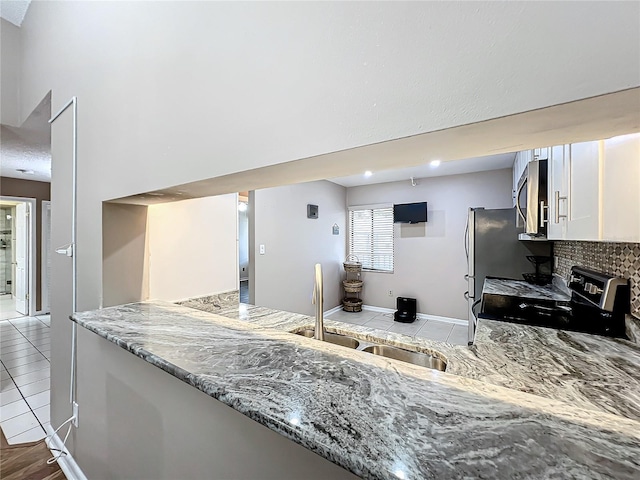 kitchen featuring sink, stainless steel appliances, white cabinets, light stone counters, and light tile patterned floors