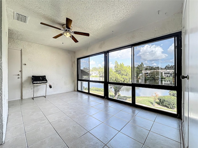 tiled empty room featuring a water view, ceiling fan, and a textured ceiling