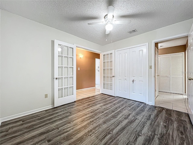 unfurnished bedroom with ceiling fan, a textured ceiling, dark hardwood / wood-style floors, a closet, and french doors