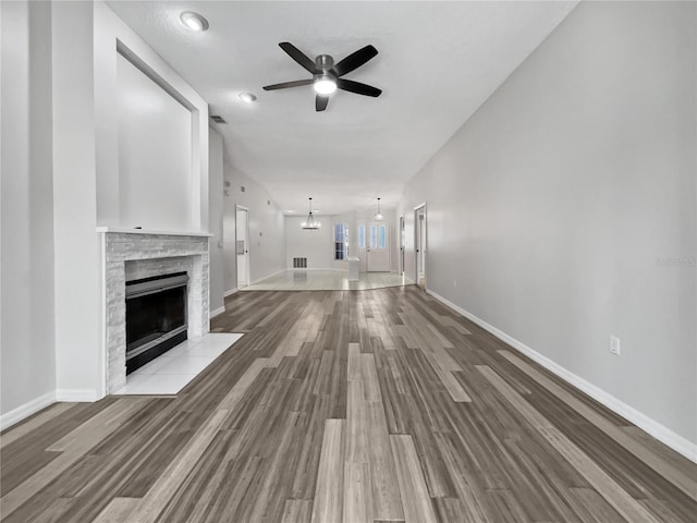 unfurnished living room featuring a tiled fireplace, light hardwood / wood-style flooring, and ceiling fan with notable chandelier