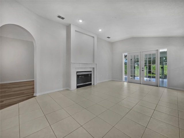 unfurnished living room with french doors, vaulted ceiling, a fireplace, and light tile patterned floors