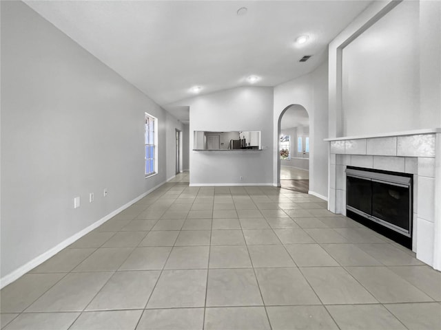 unfurnished living room featuring a tiled fireplace, light tile patterned flooring, and vaulted ceiling