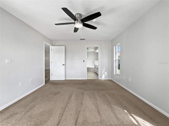 interior space with light carpet, ceiling fan, a textured ceiling, a spacious closet, and connected bathroom