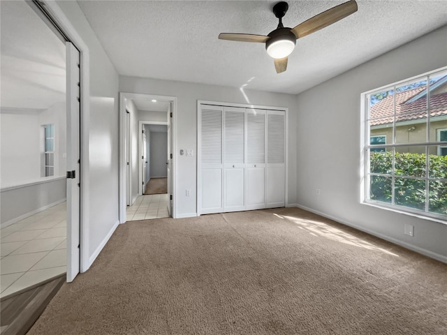 unfurnished bedroom with a closet, a textured ceiling, light colored carpet, and ceiling fan