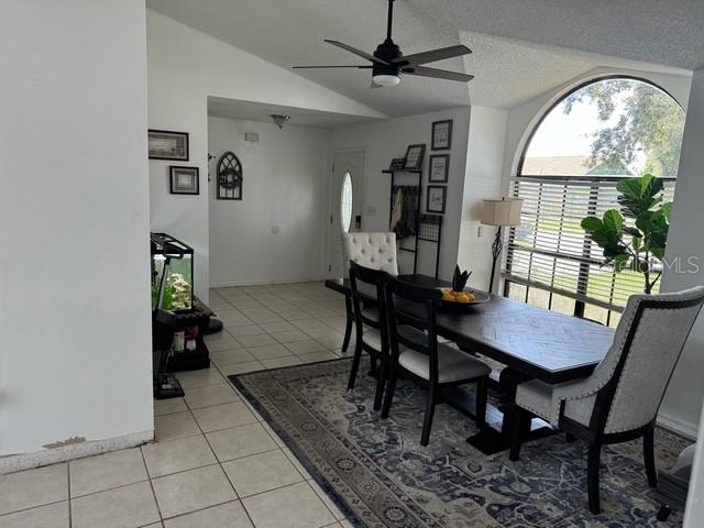 dining space with vaulted ceiling, ceiling fan, a textured ceiling, and light tile patterned floors