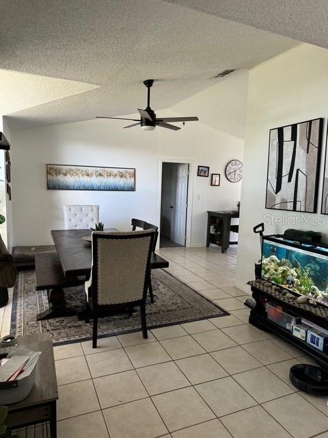 dining space featuring ceiling fan, high vaulted ceiling, a textured ceiling, and light tile patterned flooring