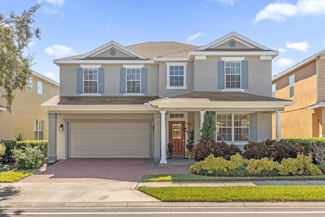 traditional-style house featuring an attached garage, a shingled roof, decorative driveway, and stucco siding