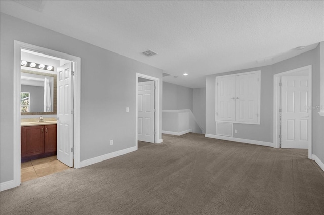 unfurnished bedroom with connected bathroom, a textured ceiling, sink, and light colored carpet