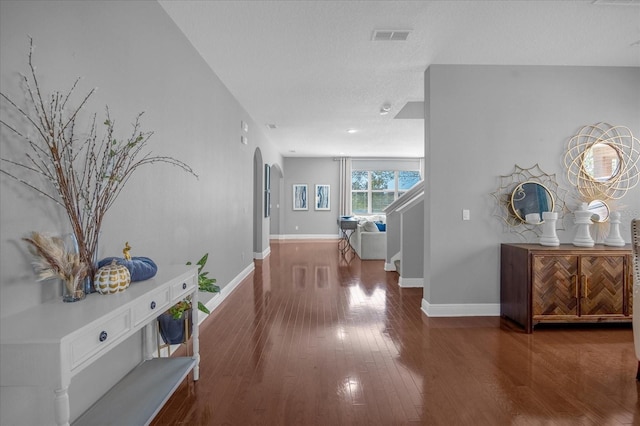 hall with arched walkways, visible vents, stairway, wood finished floors, and baseboards