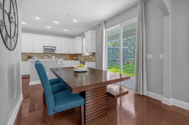 dining area featuring arched walkways, dark wood-style flooring, recessed lighting, and baseboards