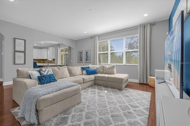 living room featuring arched walkways, recessed lighting, baseboards, and wood finished floors