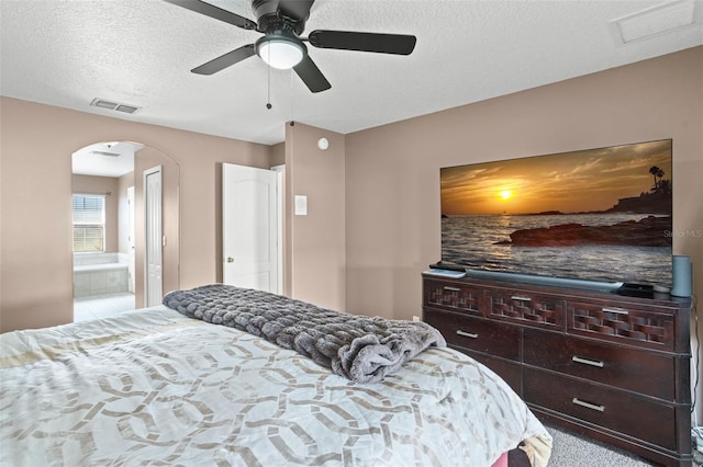 bedroom with a textured ceiling, light colored carpet, connected bathroom, and ceiling fan