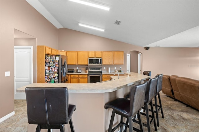 kitchen featuring a kitchen breakfast bar, a large island with sink, stainless steel appliances, and vaulted ceiling